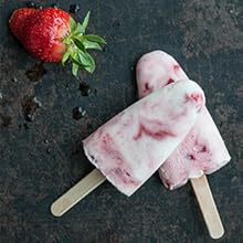 Two tasty strawberry-chia ice pops on a grey stone table with a bright red strawberry.