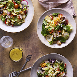 three bowls of pasta salad with rotini pasta and vegetables on a table