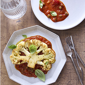 white plate with a large slice of cauliflower sitting in a pool of tomato sauce